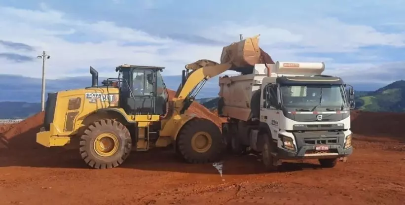 A foto mostra uma carregadeira carregando um caminhão basculante da empresa Skavaminas