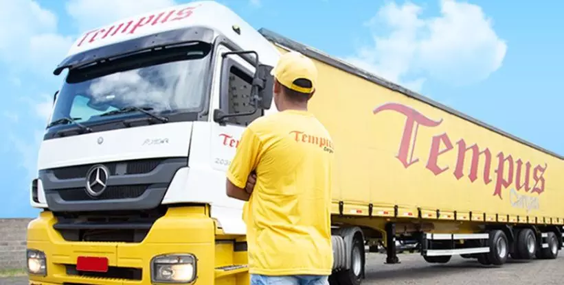A foto mostra uma carreta e um funcionário da empresa Tempus Cargas