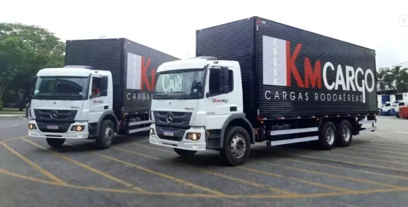 A foto mostra dois caminhões 6x2 baú da empresa KM Cargo