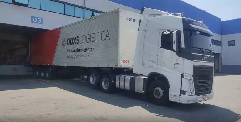 A foto mostra uma carreta da Doxs Logística estacionada no pátio da transportadora