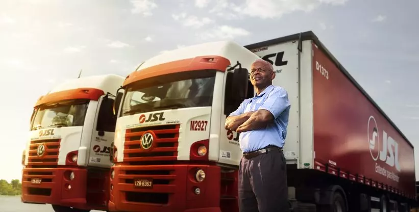 A foto mostra um motorista e dois caminhões da JSL