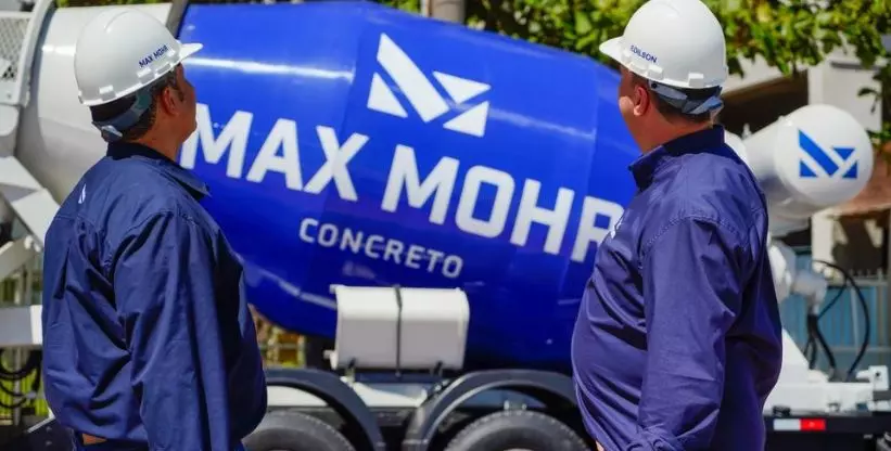 A foto mostra dois homens olhando para um caminhão betoneira da empresa MAX MOHR