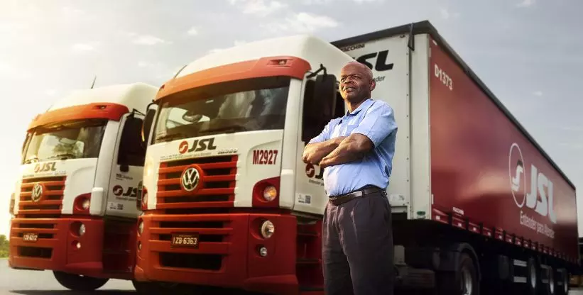 A foto mostra um motorista e duas carretas da JSL Transportes