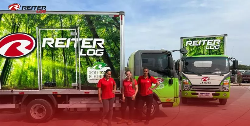 A foto mostra 2 caminhões elétricos da Reiter Log e 3 motoristas mulheres
