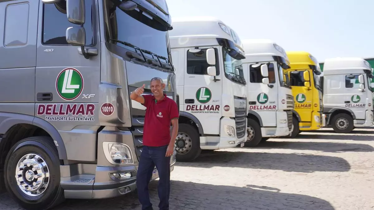 A foto mostra uma frota de caminhões e um motorista da Dellmar Transportes